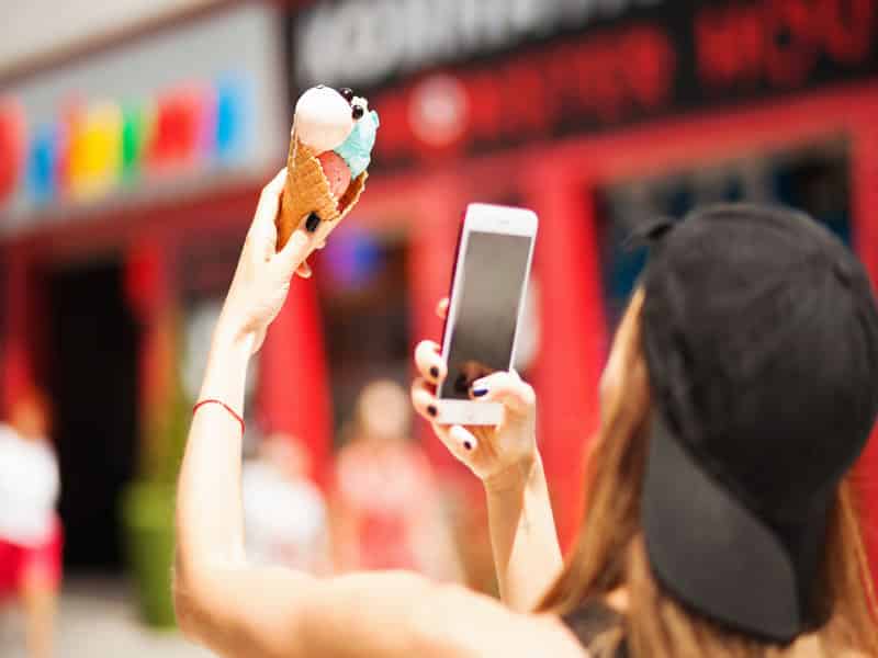 fille avec une casquette qui prend une photo de sa glace avec son smartphone pour instagram