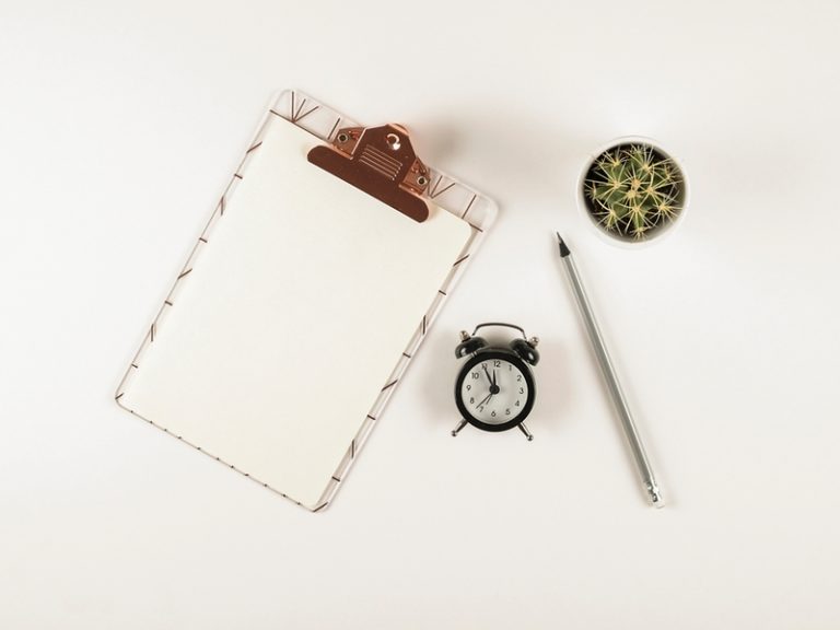 réveil, crayon, plante vert et calepin disposés sur un fond blanc