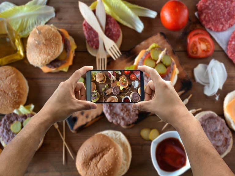 smartphone tenu par deux mains et prenant une photo de nourriture depuis le dessus