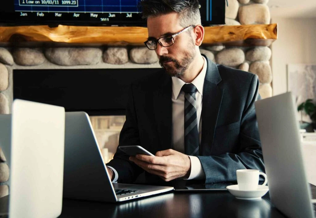 A business man sitting at his desk using his phone and his laptop to see how his website can be improved