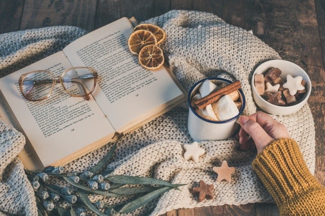 A desk scene featuring a book, a mug of marshmallows, and some handmade items.