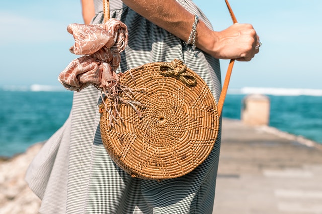 A woman wearing a grey skirt and a brown rattan bag standing by the ocean