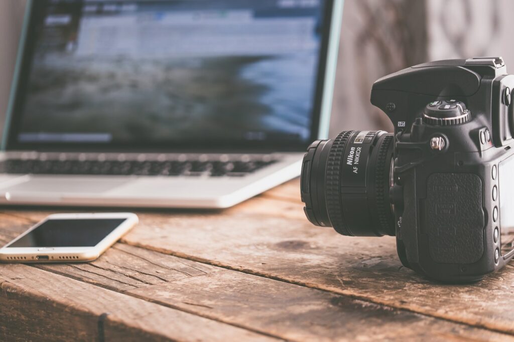 A camera and a smartphone on a desk with a laptop