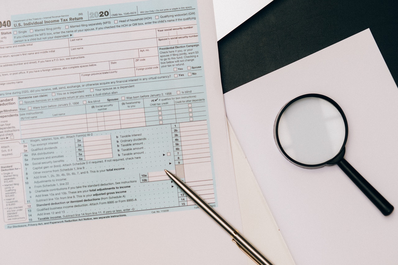 Tax forms on a table with a magnifying glass and a pen