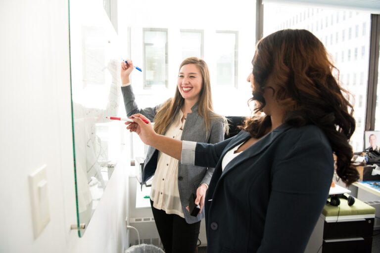 two women planning at a white-board by christina morillo